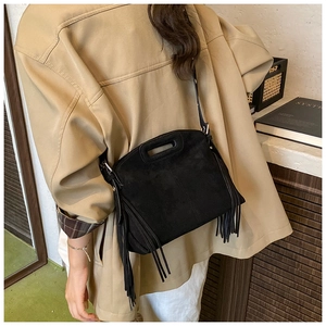Detail of black suede bag featuring decorative side tassels and unique hollow handle design
