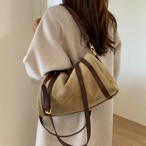 Détail d'un grand sac en daim avec lanières en cuir et boucle dorée sur un modèle