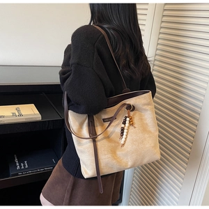 Detail of minimalist beige tote bag with suede texture and beaded charm accessory