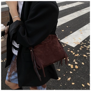 Detail of dark burgundy faux suede crossbody bag with long fringes in autumn street style