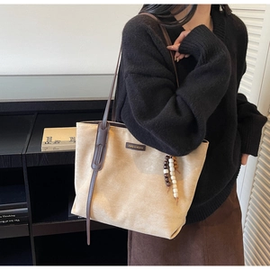 Detail of beige tote bag featuring brown leather straps and ethnic wooden bead charm