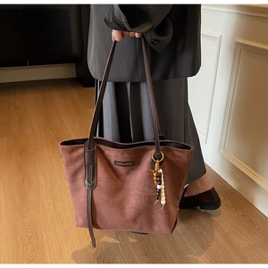 Detailed close-up of dark brown suede tote bag with ethnic beaded charm and brand logo