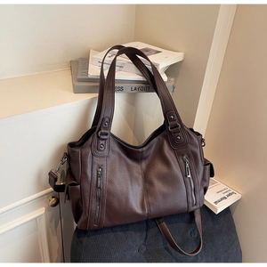 Detail of dark brown lychee leather tote bag featuring dual vertical zipper accents and straps