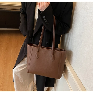 Brown lychee leather tote bag worn by a model in a professional blazer suit