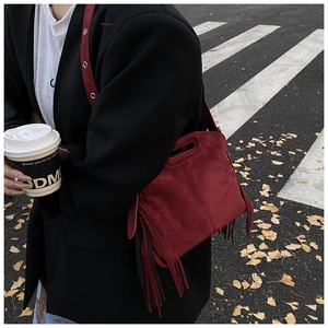 Detail of burgundy faux suede crossbody bag with fringe tassel in outdoor autumn setting