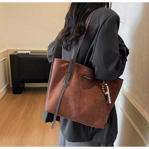 Close-up of brown suede tote bag with leather handles and decorative beaded tassel charm