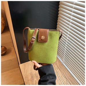 Close-up of grass green suede bucket bag with brown leather flap and golden metal buckle