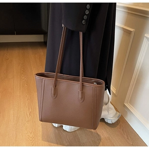 Detailed macro view of deep brown litchi grain leather texture on a spacious tote bag