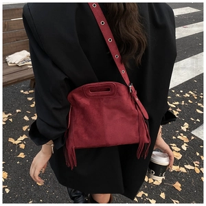 Outdoor view of a dark red matte leather tassel crossbody bag worn with a black coat