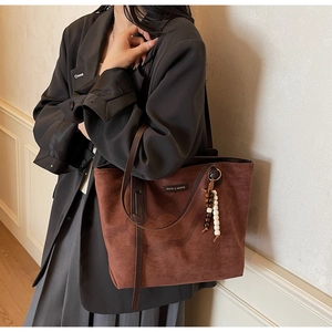 Detail of a large brown suede tote bag with stylish beaded tassel and long shoulder straps