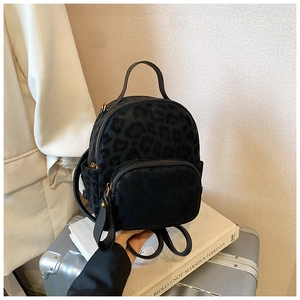 Detailed close-up of dark leopard print mini backpack with gold hardware on a travel suitcase