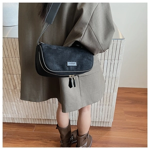 Close-up of black suede moon bag worn with grey blazer for a minimalist retro look