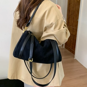 Détail du sac polochon en daim noir avec bandoulière cuir et boucles dorées sur modèle