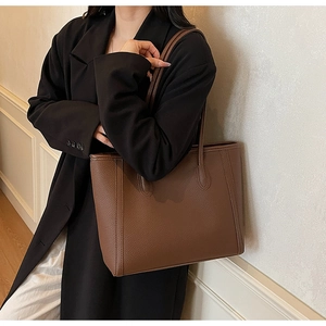 Detail of dark brown tote bag with lychee texture and slim straps on a model