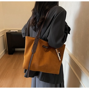 Detail of tan suede tote bag featuring a brand label and vintage beaded charm