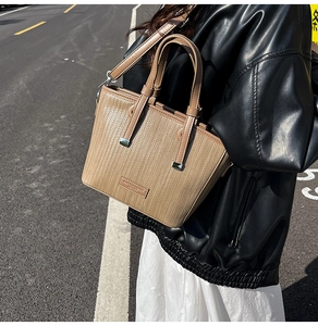 Close-up of khaki woven bucket bag with metal logo and detachable leather strap in street style