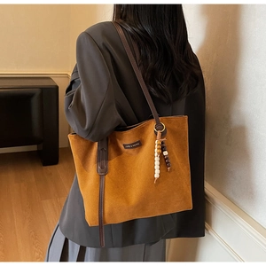 Brown faux suede tote bag with leather straps and wooden bead tassel shown on model