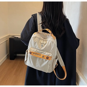 Detail of nylon backpack featuring orange straps with blue floral motifs and logo