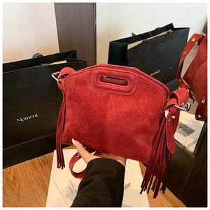 Detail of red matte suede handbag featuring decorative long side tassels and handle