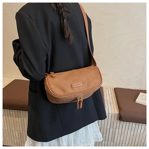 Brown suede cylindrical crossbody bag with metal zippers shown on a model's shoulder