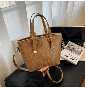Detail of tan woven tote bag with dual handles and long shoulder strap in a desk setup