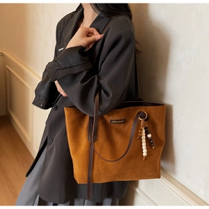 Close-up of brown suede tote bag featuring metallic logo and beaded charm on the side