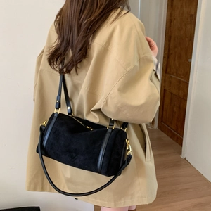Détail du sac polochon en daim noir avec ferrures dorées porté par un mannequin chic