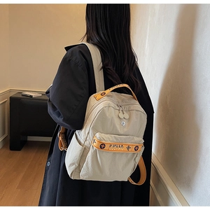 Detail of light beige nylon backpack with orange contrast straps and multi-pocket design