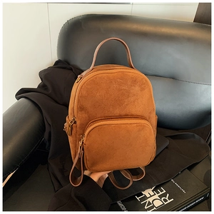 Detail view of brown suede backpack with gold zippers on a black leather sofa