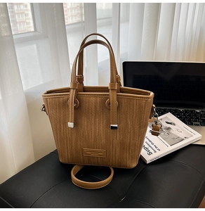 Detail of woven brown bucket bag featuring dual leather handles and adjustable shoulder strap