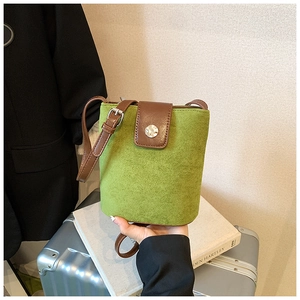 Detailed view of the green suede bucket bag featuring contrast brown leather and metal buckle