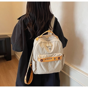 Close-up of beige nylon backpack with orange floral embroidery on the shoulder straps