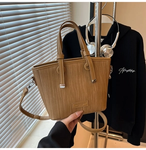 Detail of woven texture tote bag with leather logo tag and adjustable shoulder strap