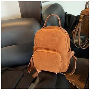 Macro detail of the brown faux suede backpack featuring golden zippers and a front pocket