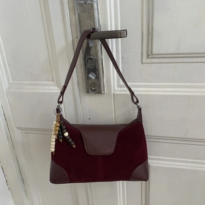 Detail view of burgundy crossbody bag with matte texture and decorative beads on a door