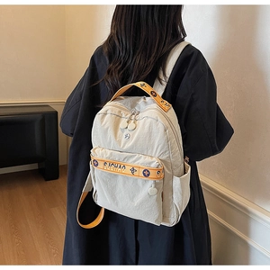 Detail of beige nylon backpack featuring orange jacquard webbing straps and side pockets