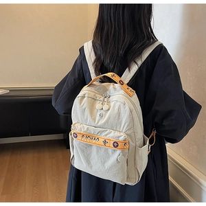 Detail view of cream nylon backpack featuring orange woven straps and zipper texture