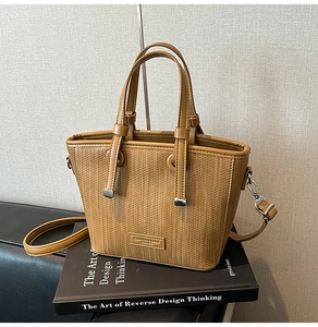Detailed view of tan woven leather texture on small bucket bag with logo plaque