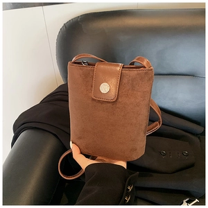 Close-up of brown suede bucket bag with round silver magnetic buckle and smooth strap