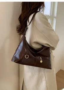 Detail of a dark brown glossy leather crescent bag with metal ring and zip pocket