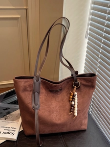 Chic brown suede tote bag with stylish beaded pendant and metallic logo on leather surface