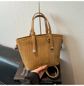 Close-up of brown woven tote bag with leather handles and metallic brand logo plate