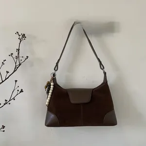 Close-up of brown faux suede shoulder bag featuring ethnic wooden bead tassel and smooth leather trim