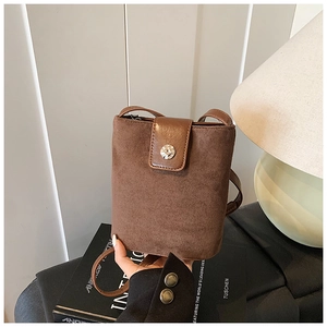 Close-up of brown suede bucket bag with leather flap and round metal buckle detail