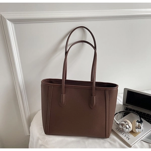 Close-up of a dark brown lychee leather tote bag shown in a professional office setting