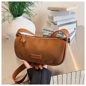 Brown suede underarm bag with leather logo detail held in a modern home setting