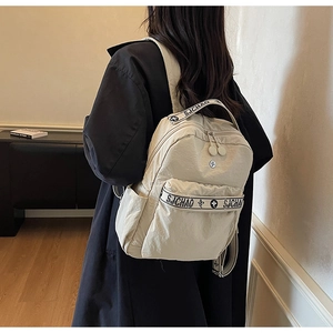 Side view of beige nylon backpack with SJCHAO lettering strap worn by model