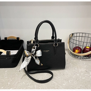 Detail of black litchi grain leather tote bag with gold logo and patterned silk scarf