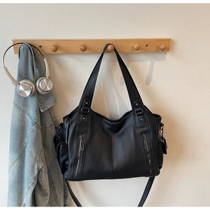 Detail of black pebbled leather tote bag with dual front zipper pockets on wooden hanger