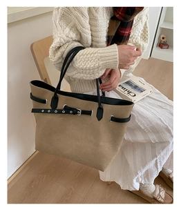 Detail of khaki frosted tote bag with black straps and metal eyelet buckles in a home setting